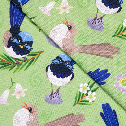 Closeup of a folded tea towel with a green, blue, yellow and beige superb fairywrens pattern.
