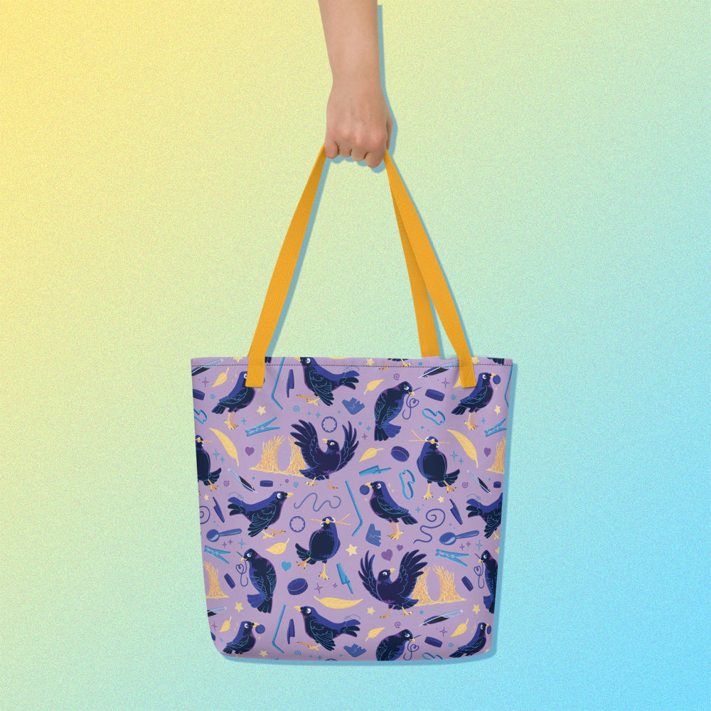 Hand holding a tote bag with yellow handles and a purple/blue/yellow satin bowerbird pattern on a yellow and blue gradient background.