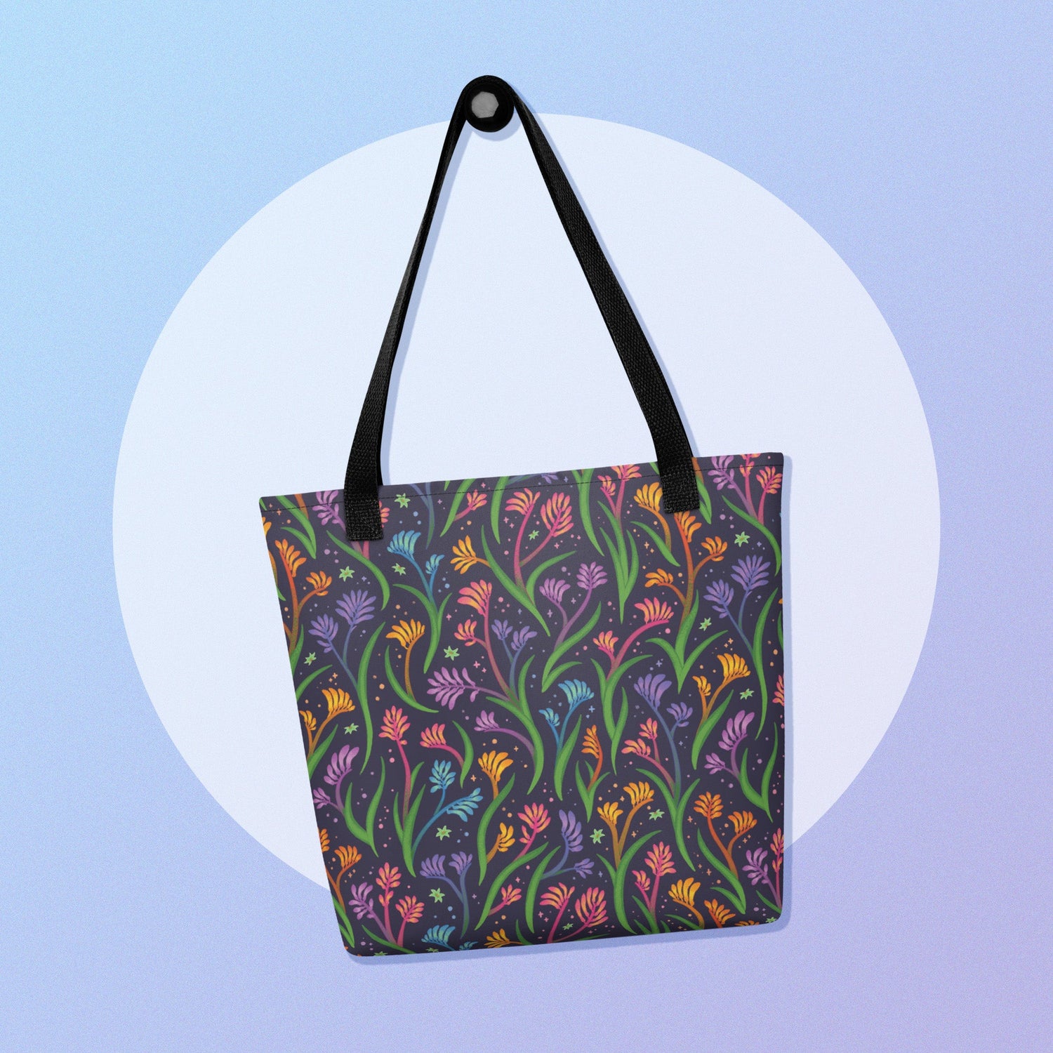 A rainbow kangaroo paw flower pattern tote bag on a white circle on a blue and purple gradient background.