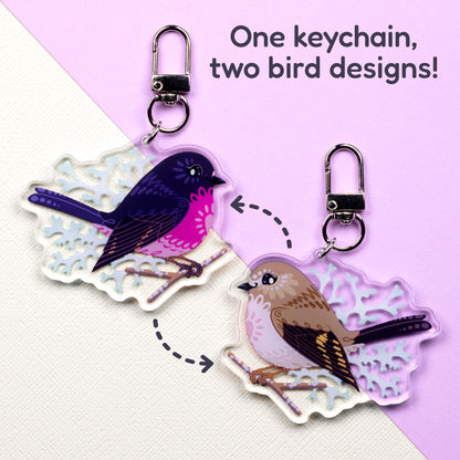 Both sides of a double-sided acrylic keychain of male & female pink robins sitting on a split cream and pale lilac background with the text 'One keychain, two bird designs!' in the top right.