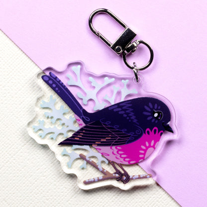 Double-sided acrylic keychain of male & female pink robins sitting on a split cream and pale lilac background.