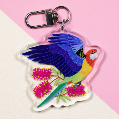 Double-sided acrylic keychain of crimson & eastern rosellas sitting on a split cream and pale pink background.