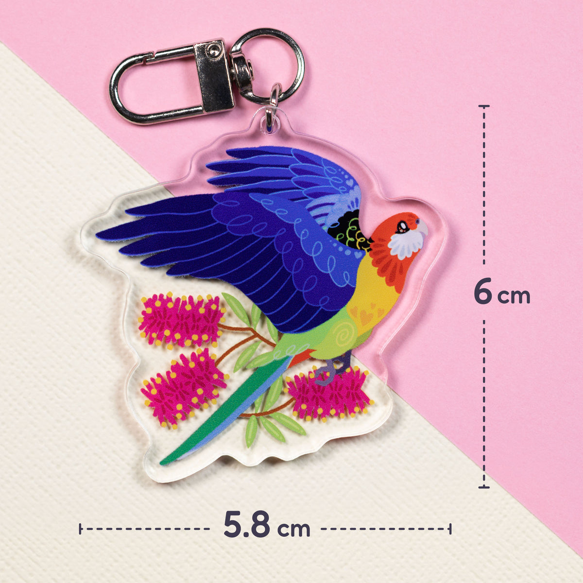 5.8x6cm double-sided acrylic keychain of crimson & eastern rosellas sitting on a split cream and pale pink background.