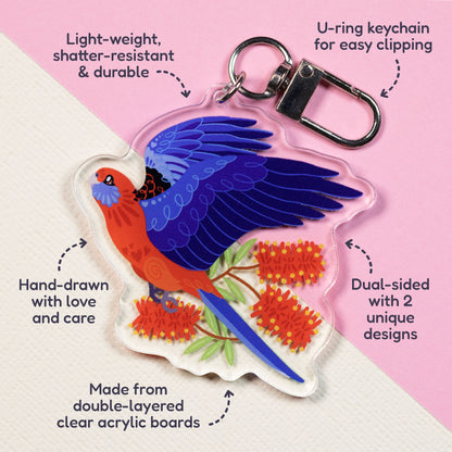 Features & benefits (U-ring keychain for easy clipping, light-weight, shatter-resistant & durable, hand-drawn with love and care, made from double-layered clear acrylic boards, dual-sided with 2 unique designs) surrounding a double-sided acrylic keychain of crimson & eastern rosellas sitting on a split cream and pale pink background.
