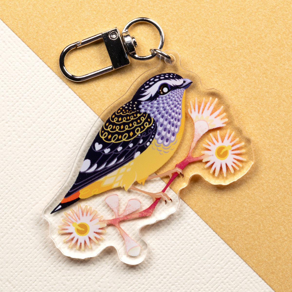 Double-sided acrylic keychain of male & female spotted pardalotes sitting on a split cream & metallic gold background. 
