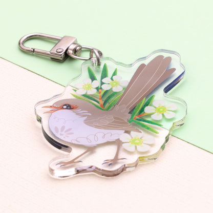 Angled photo of a double-sided acrylic keychain of a male and female superb fairywren sitting on a split cream and pale green background.