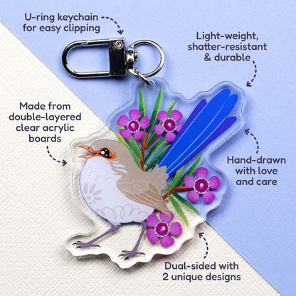 Features & benefits (U-ring keychain for easy clipping, light-weight, shatter-resistant & durable, hand-drawn with love and care, made from double-layered clear acrylic boards, dual-sided with 2 unique designs) surrounding a double-sided acrylic keychain of male & female splendid fairywrens sitting on a split cream and pale blue background.