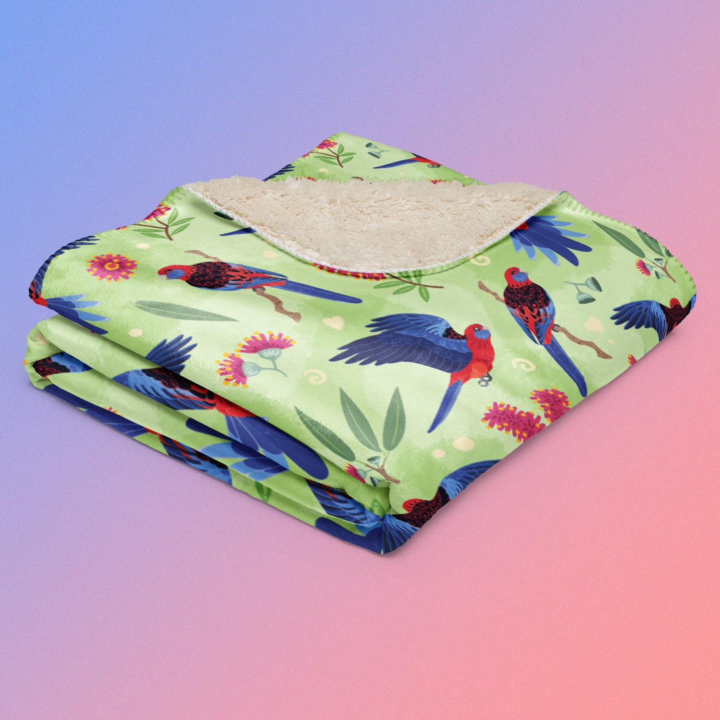 A folded green, red and blue crimson rosella & native Aussie plant pattern blanket on a blue and pink gradient background.
