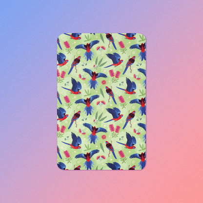 A green, red and blue crimson rosella & native Aussie plant pattern blanket on a blue and pink gradient background.