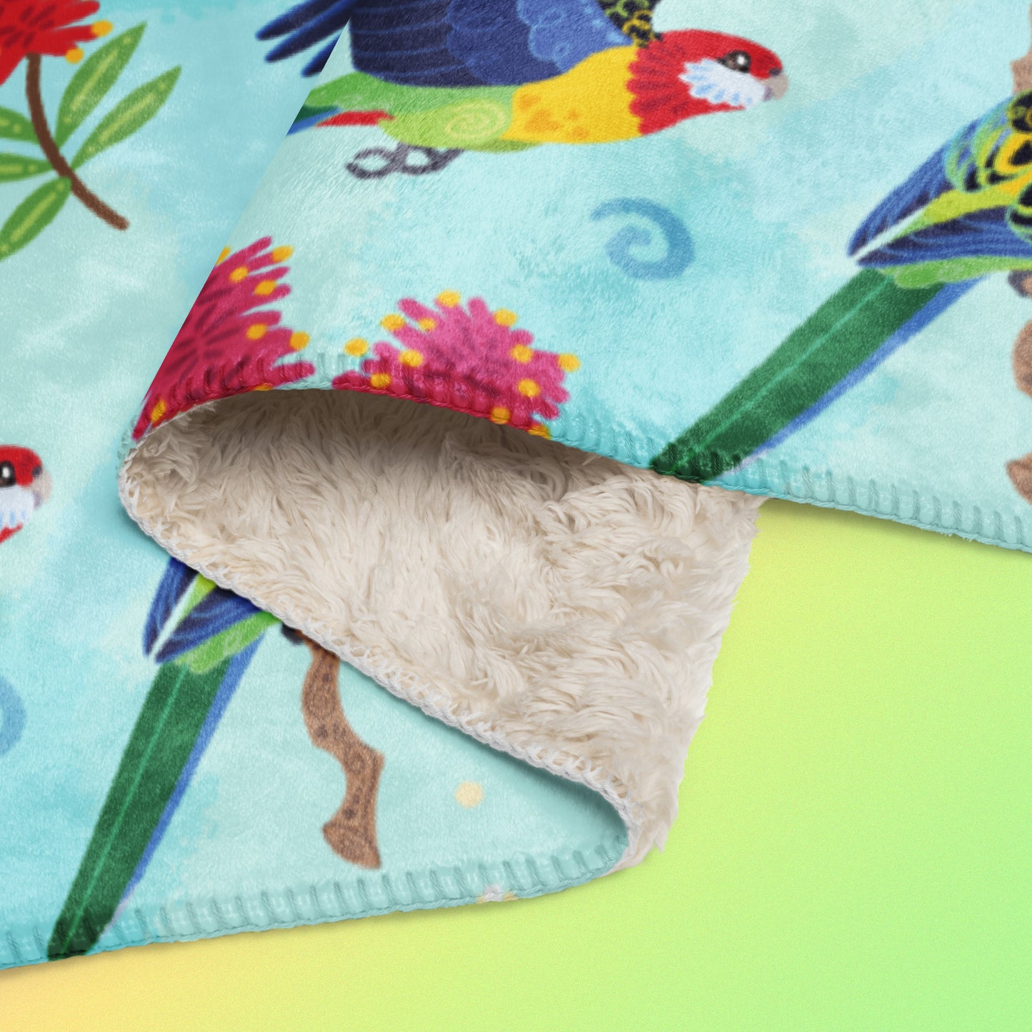 Close up detail of a folded blue, pink and green eastern rosella & native Aussie plant pattern blanket on a pink, yellow and green gradient background.