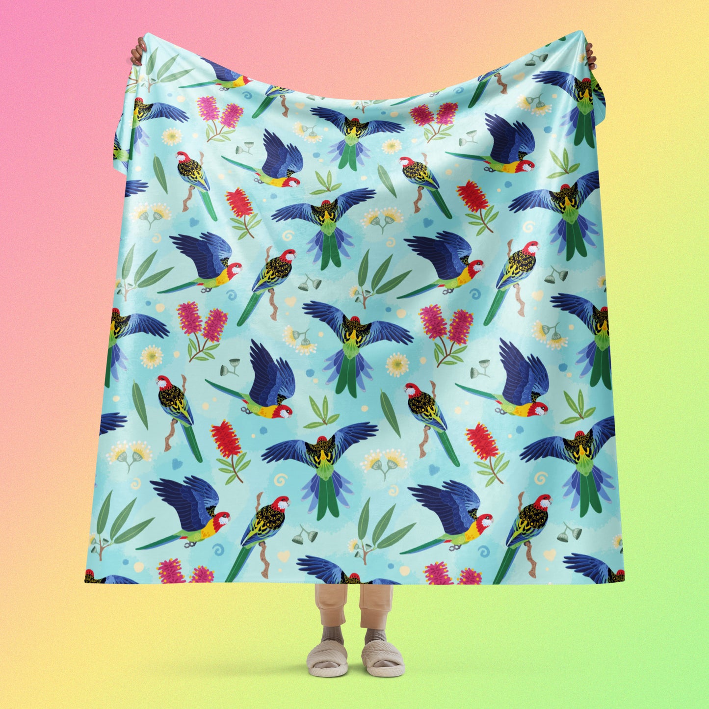 Person holding a blue, pink and green eastern rosella & native Aussie plant pattern blanket above their head on a pink, yellow and green gradient background.
