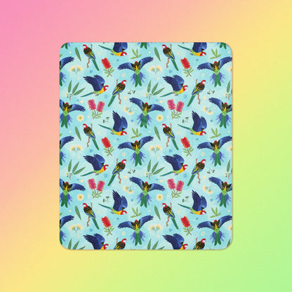 A blue, pink and green eastern rosella & native Aussie plant pattern blanket on a pink, yellow and green gradient background.