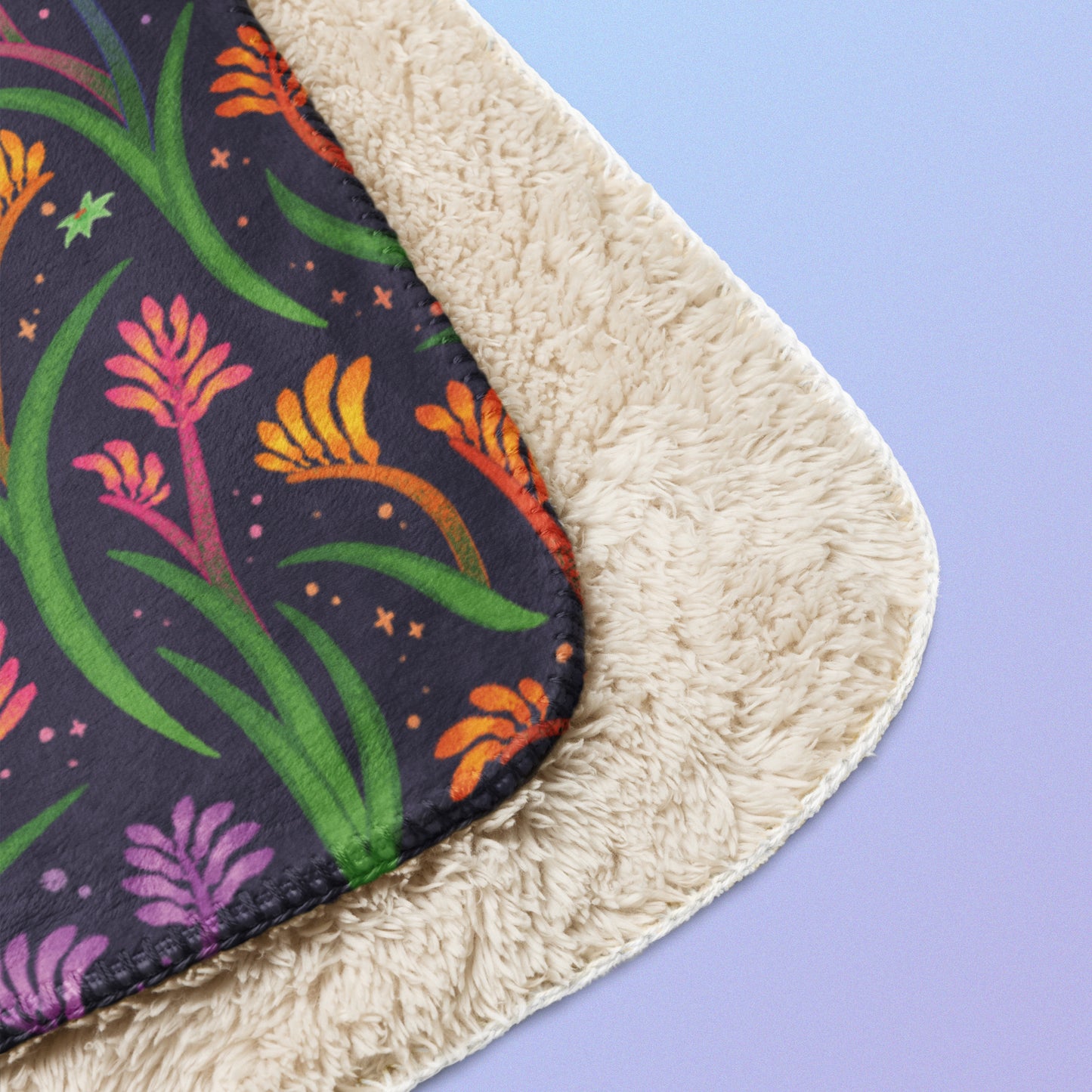 Close up detail of a folded rainbow kangaroo paw flower pattern blanket on a blue and purple gradient background.