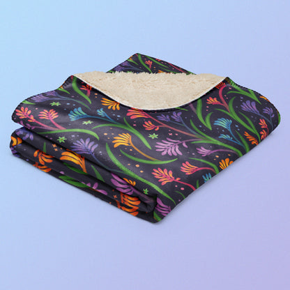 A folded rainbow kangaroo paw flower pattern blanket on a blue and purple gradient background.