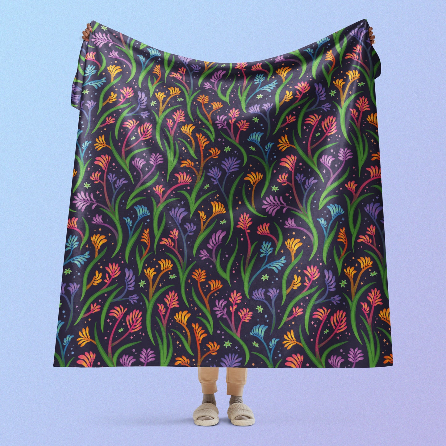 Person holding a rainbow kangaroo paw flower pattern blanket above their head on a blue and purple gradient background.