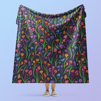 Person holding a rainbow kangaroo paw flower pattern blanket above their head on a blue and purple gradient background.