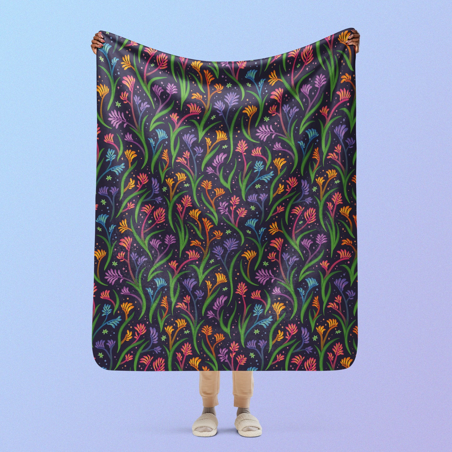 Person holding a rainbow kangaroo paw flower pattern blanket above their head on a blue and purple gradient background.