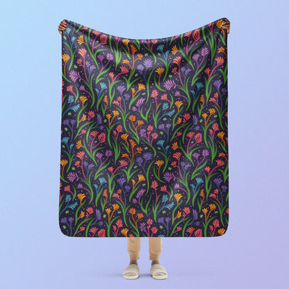 Person holding a rainbow kangaroo paw flower pattern blanket above their head on a blue and purple gradient background.