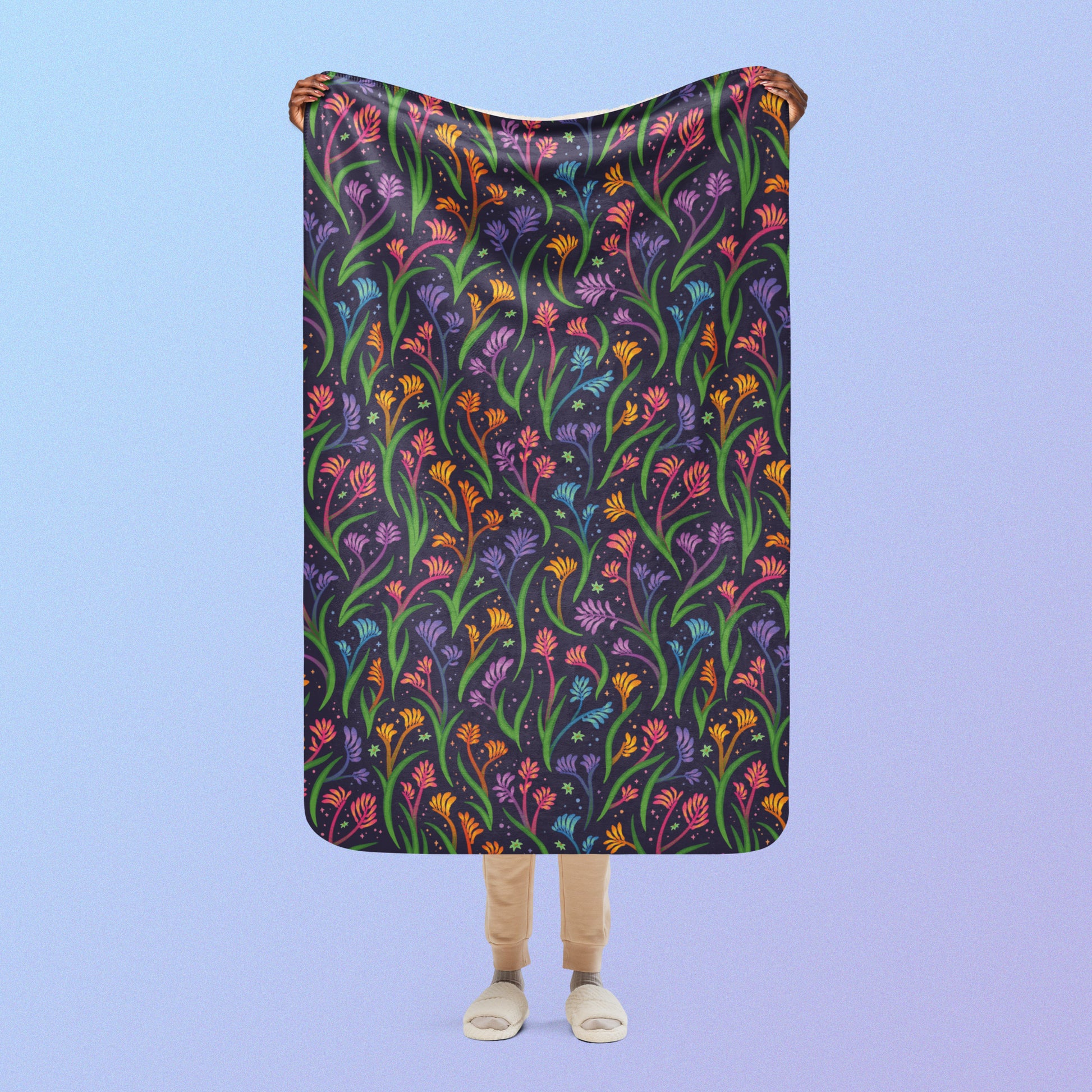 Person holding a rainbow kangaroo paw flower pattern blanket above their head on a blue and purple gradient background.