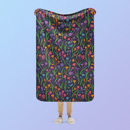 Person holding a rainbow kangaroo paw flower pattern blanket above their head on a blue and purple gradient background.