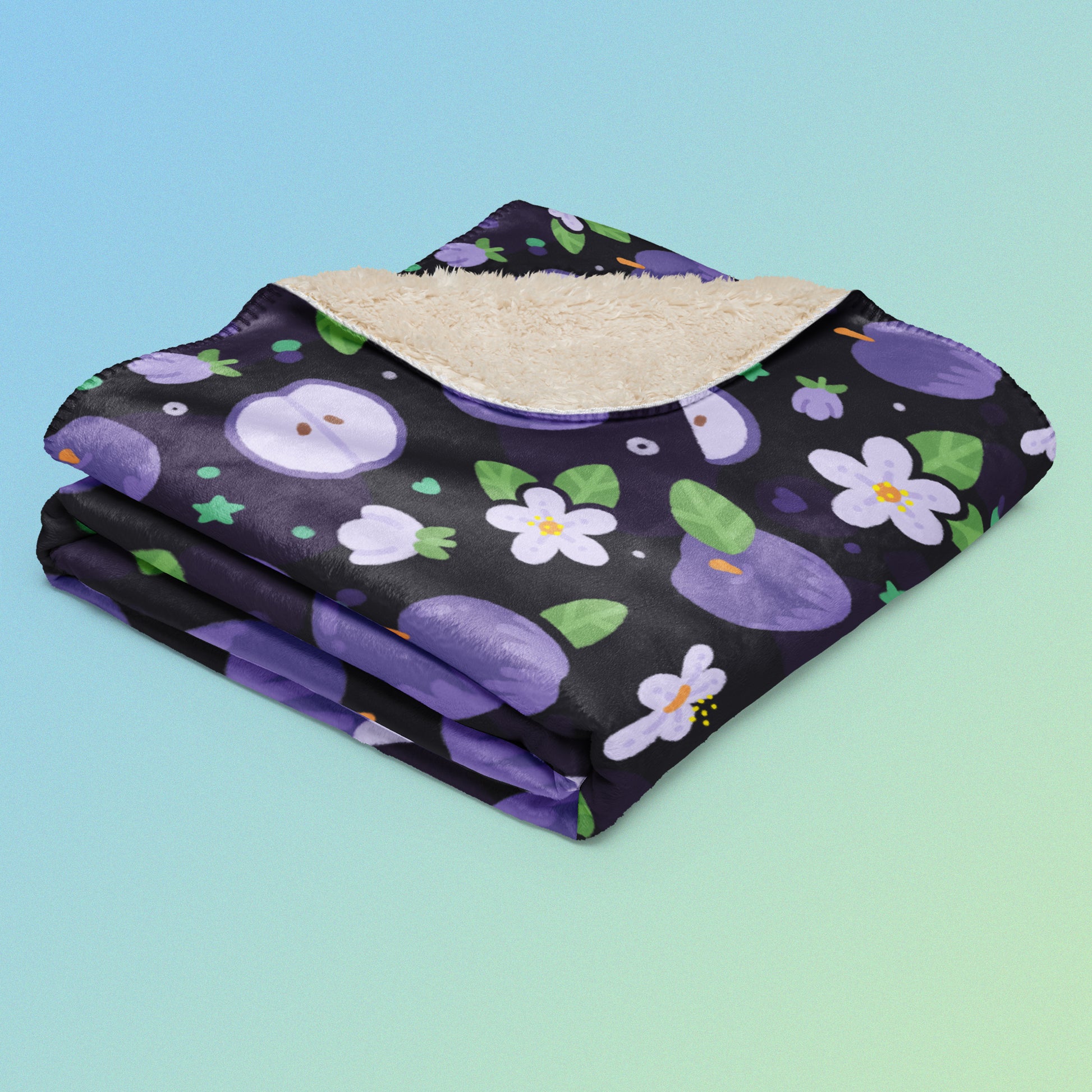 A folded purple apples & blossoms pattern blanket on a blue and green gradient background.