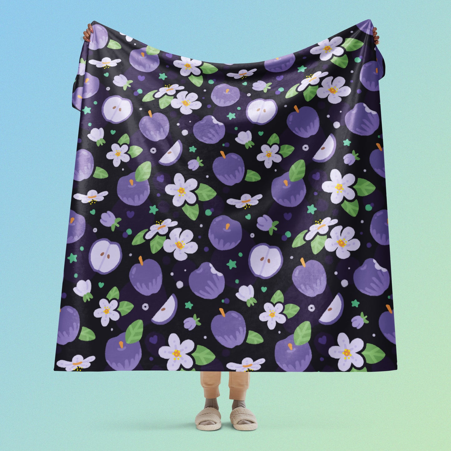 Person holding a purple apples & blossoms pattern blanket above their head on a blue and green gradient background.