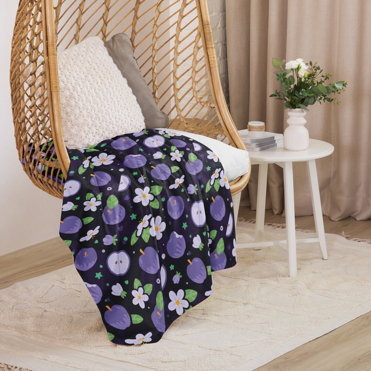 A purple apples & blossoms pattern blanket sitting on a swinging woven egg chair with soft, natural lighting.