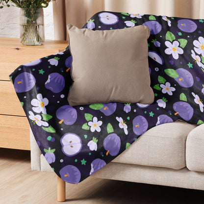 A purple apples & blossoms pattern blanket sitting on a beige sofa with a beige pillow on top.