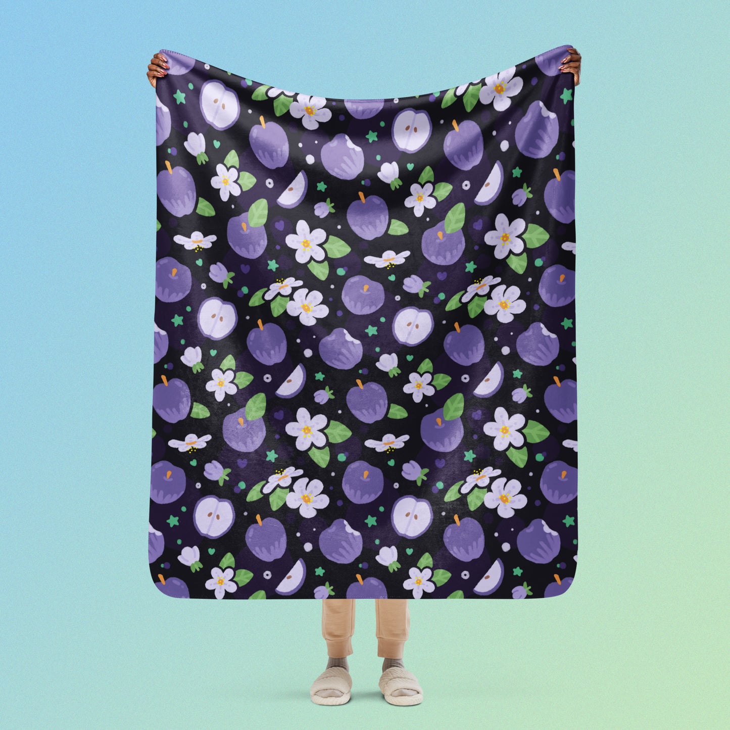 Person holding a purple apples & blossoms pattern blanket above their head on a blue and green gradient background.