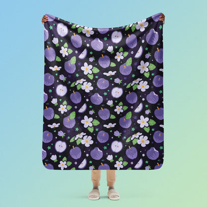 Person holding a purple apples & blossoms pattern blanket above their head on a blue and green gradient background.