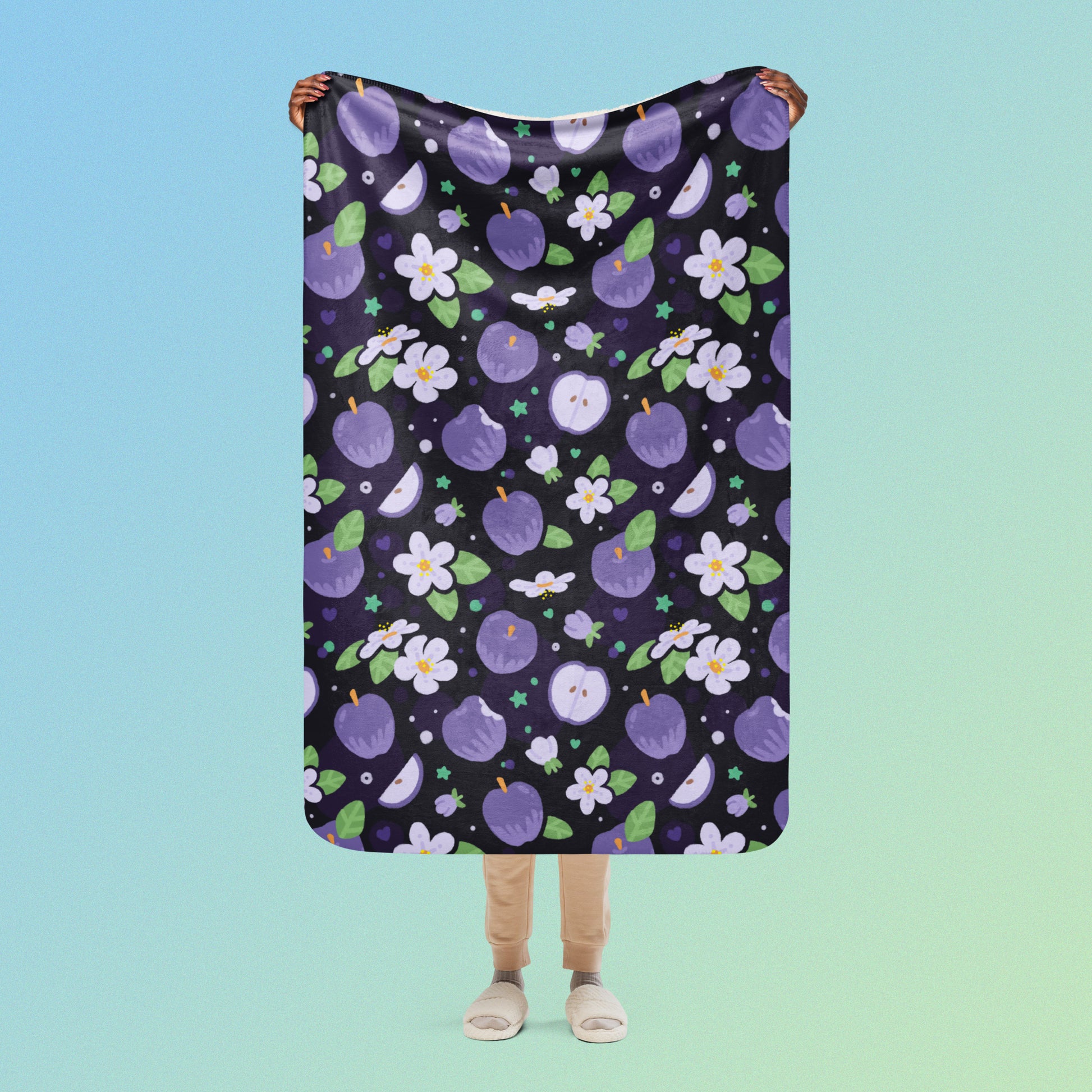 Person holding a purple apples & blossoms pattern blanket above their head on a blue and green gradient background.