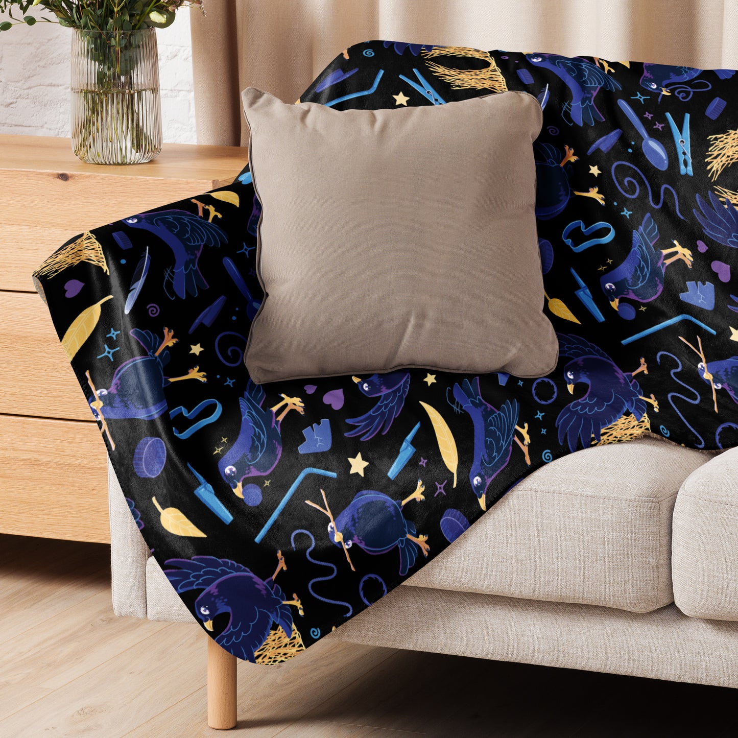 A black, blue, purple and yellow male Aussie satin bowerbird pattern blanket sitting on a beige sofa with a beige pillow on top.
