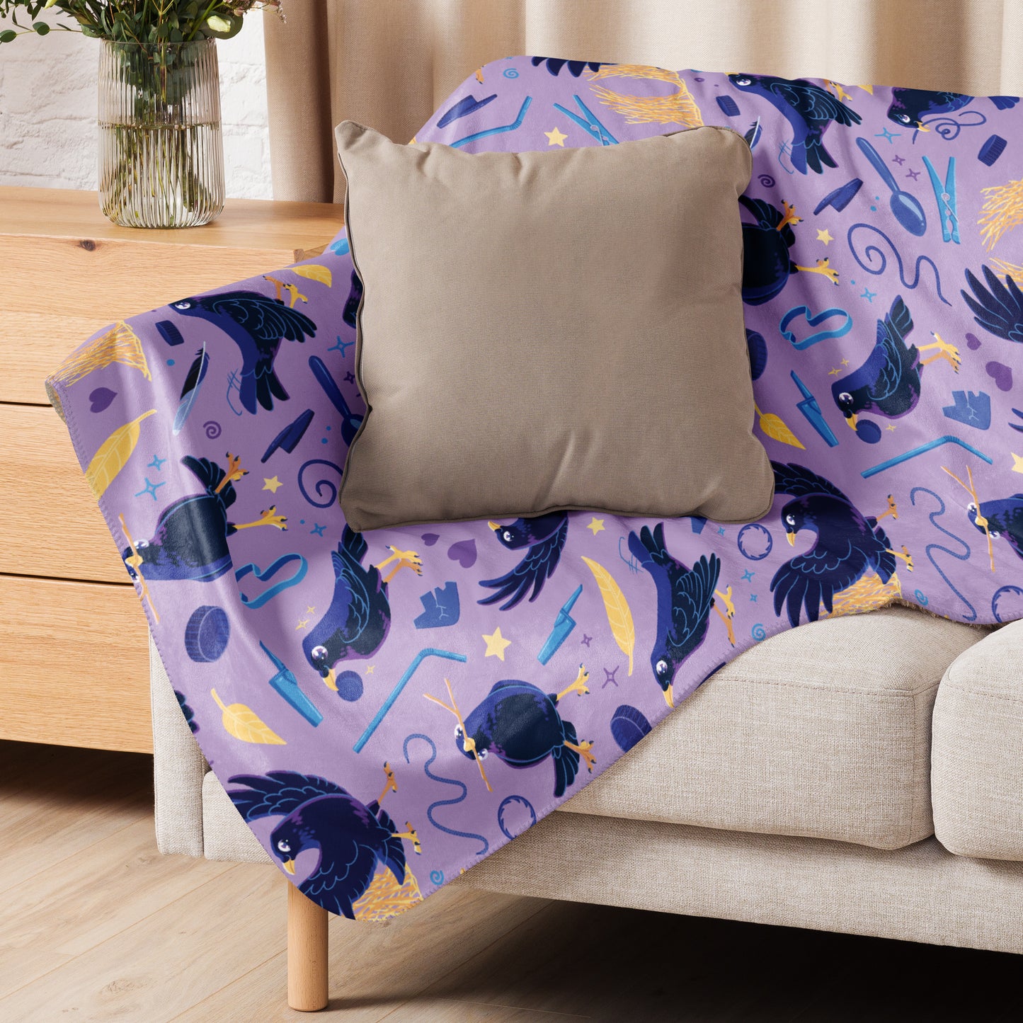 A purple, blue and yellow male Aussie satin bowerbird pattern blanket sitting on a beige sofa with a beige pillow on top.