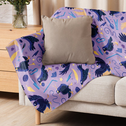 A purple, blue and yellow male Aussie satin bowerbird pattern blanket sitting on a beige sofa with a beige pillow on top.