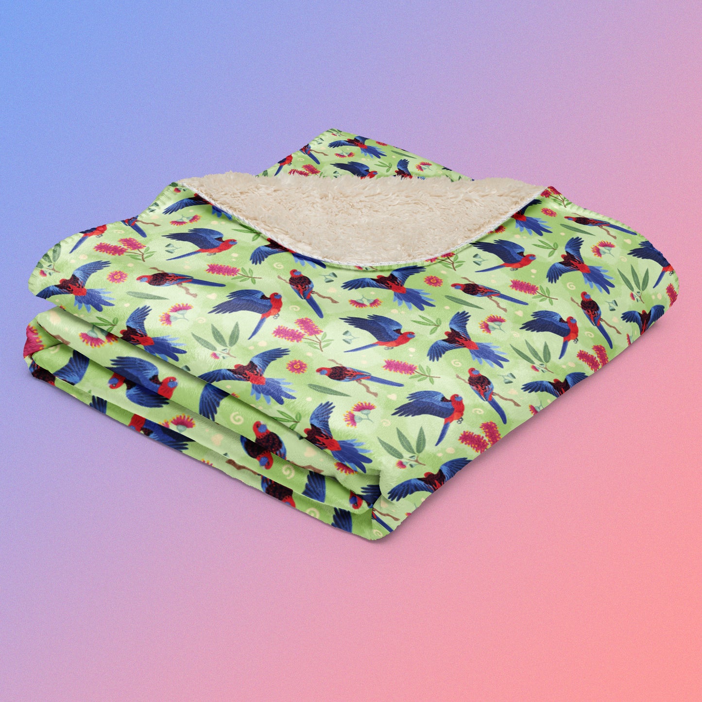 A folded green, red and blue crimson rosella & native Aussie plant pattern blanket on a blue and pink gradient background.