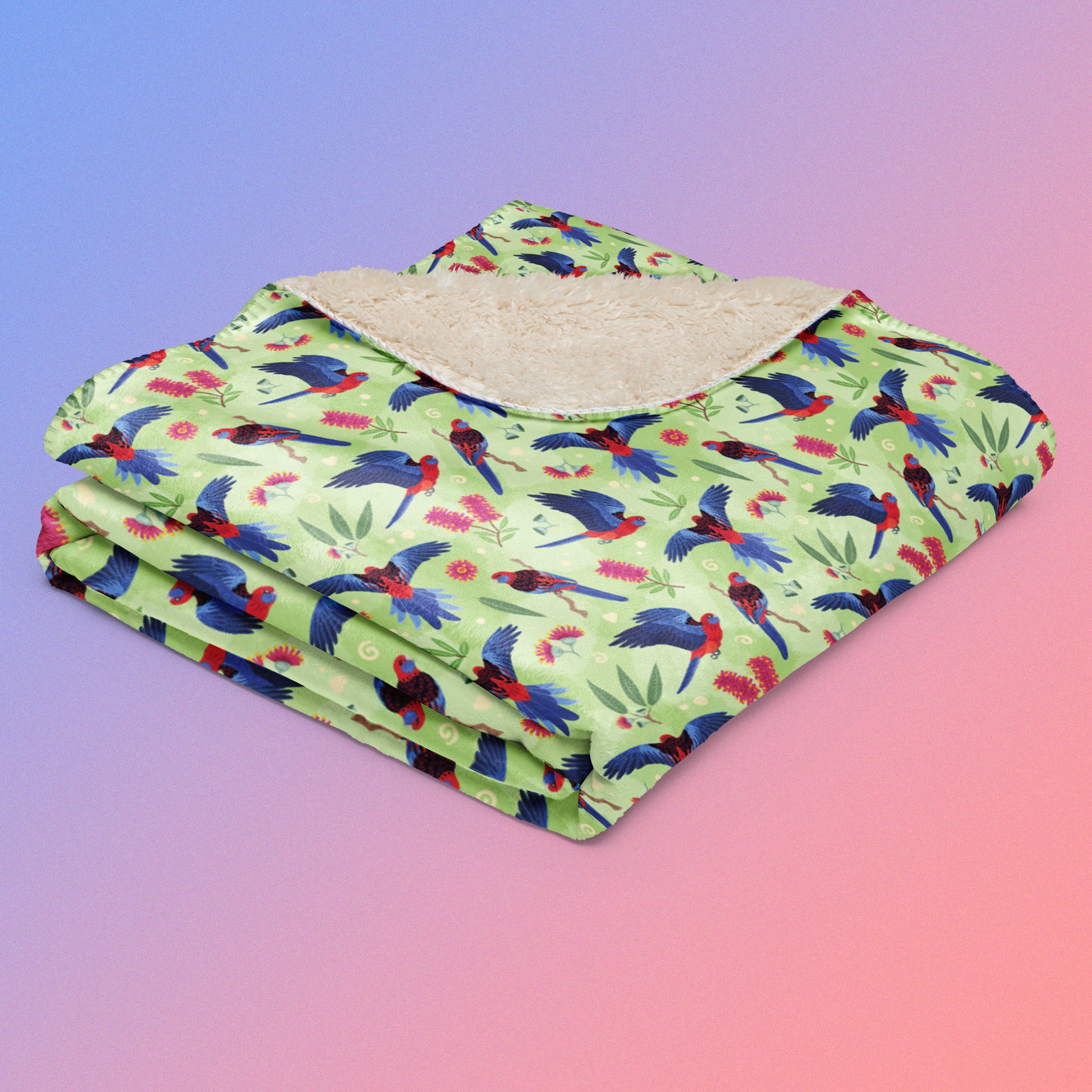 A folded green, red and blue crimson rosella & native Aussie plant pattern blanket on a blue and pink gradient background.