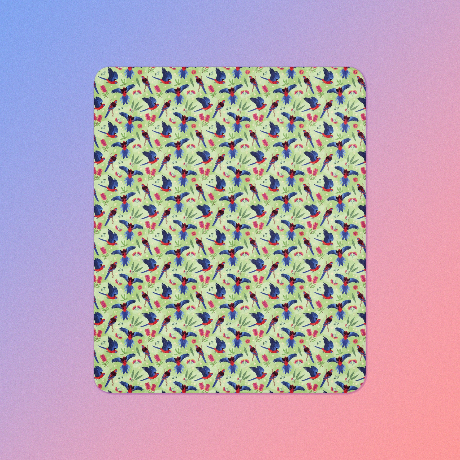 A green, red and blue crimson rosella & native Aussie plant pattern blanket on a blue and pink gradient background.