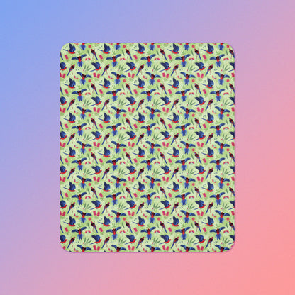 A green, red and blue crimson rosella & native Aussie plant pattern blanket on a blue and pink gradient background.