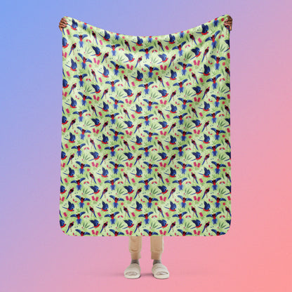 Person holding a green, red and blue crimson rosella & native Aussie plant pattern blanket above their head on a blue and pink gradient background.