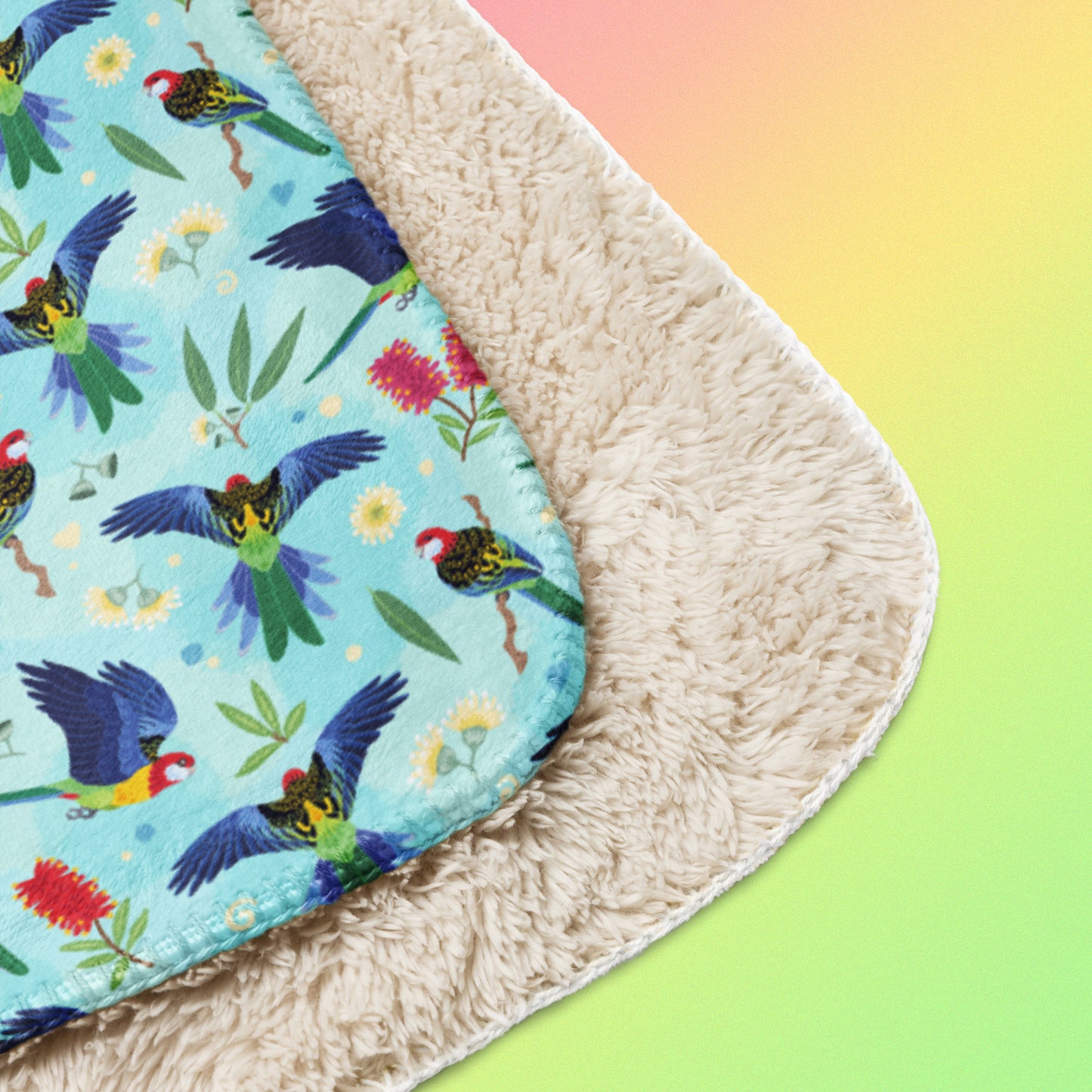Close up detail of a folded blue, pink and green eastern rosella & native Aussie plant pattern blanket on a pink, yellow and green gradient background.