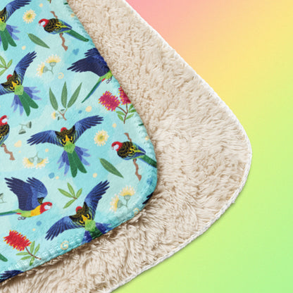 Close up detail of a folded blue, pink and green eastern rosella & native Aussie plant pattern blanket on a pink, yellow and green gradient background.
