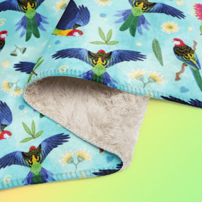 Close up detail of a folded blue, pink and green eastern rosella & native Aussie plant pattern blanket on a pink, yellow and green gradient background.
