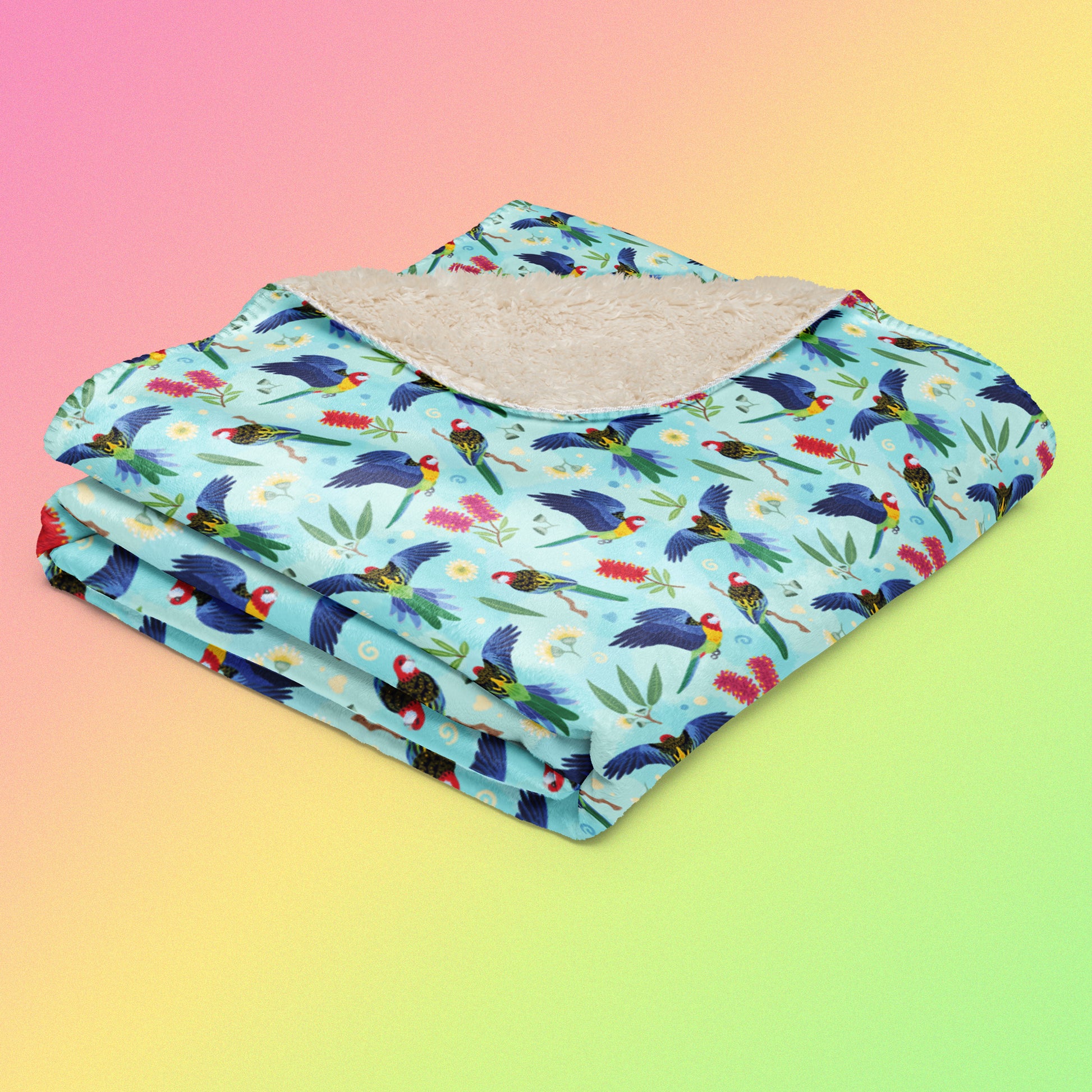 A folded blue, pink and green eastern rosella & native Aussie plant pattern blanket on a pink, yellow and green gradient background.