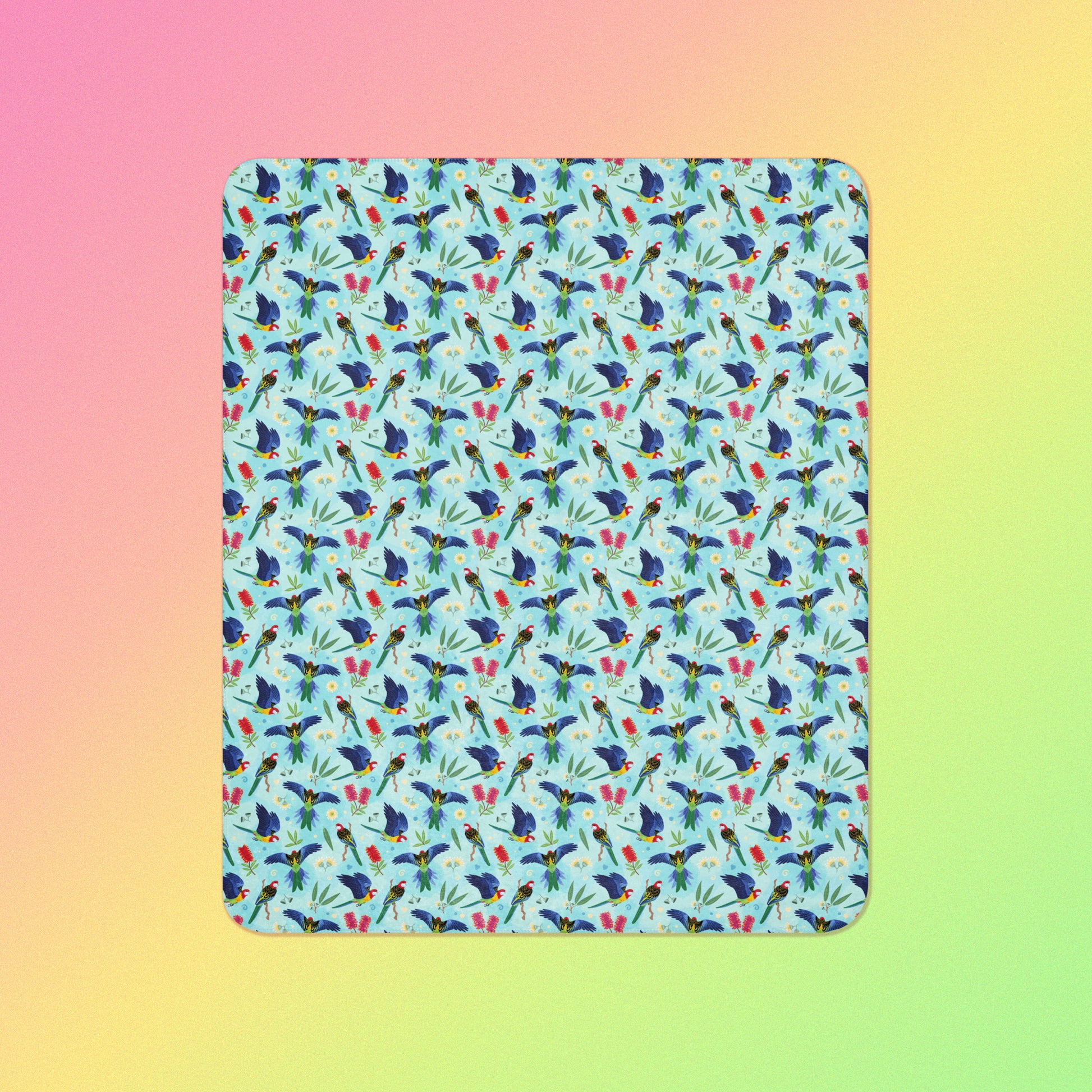 A blue, pink and green eastern rosella & native Aussie plant pattern blanket on a pink, yellow and green gradient background.