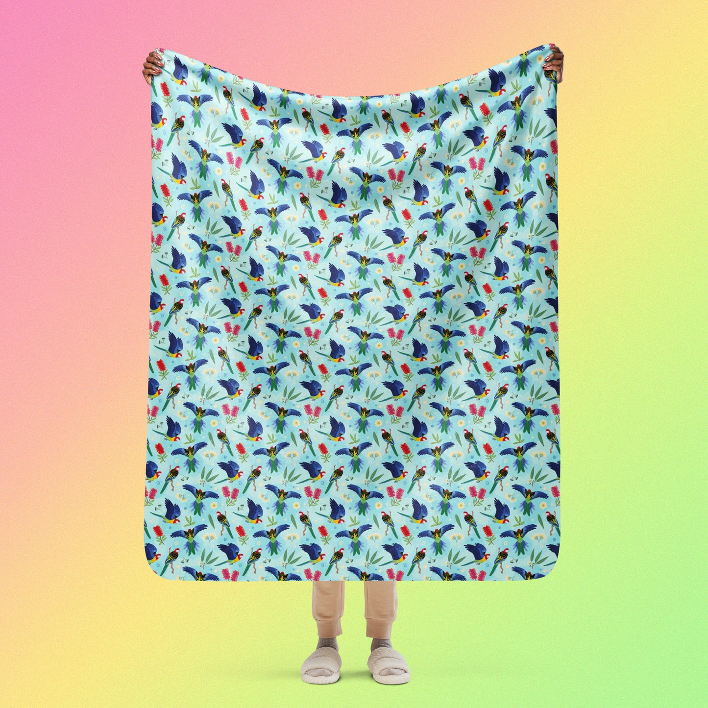 Person holding a blue, pink and green eastern rosella & native Aussie plant pattern blanket above their head on a pink, yellow and green gradient background.