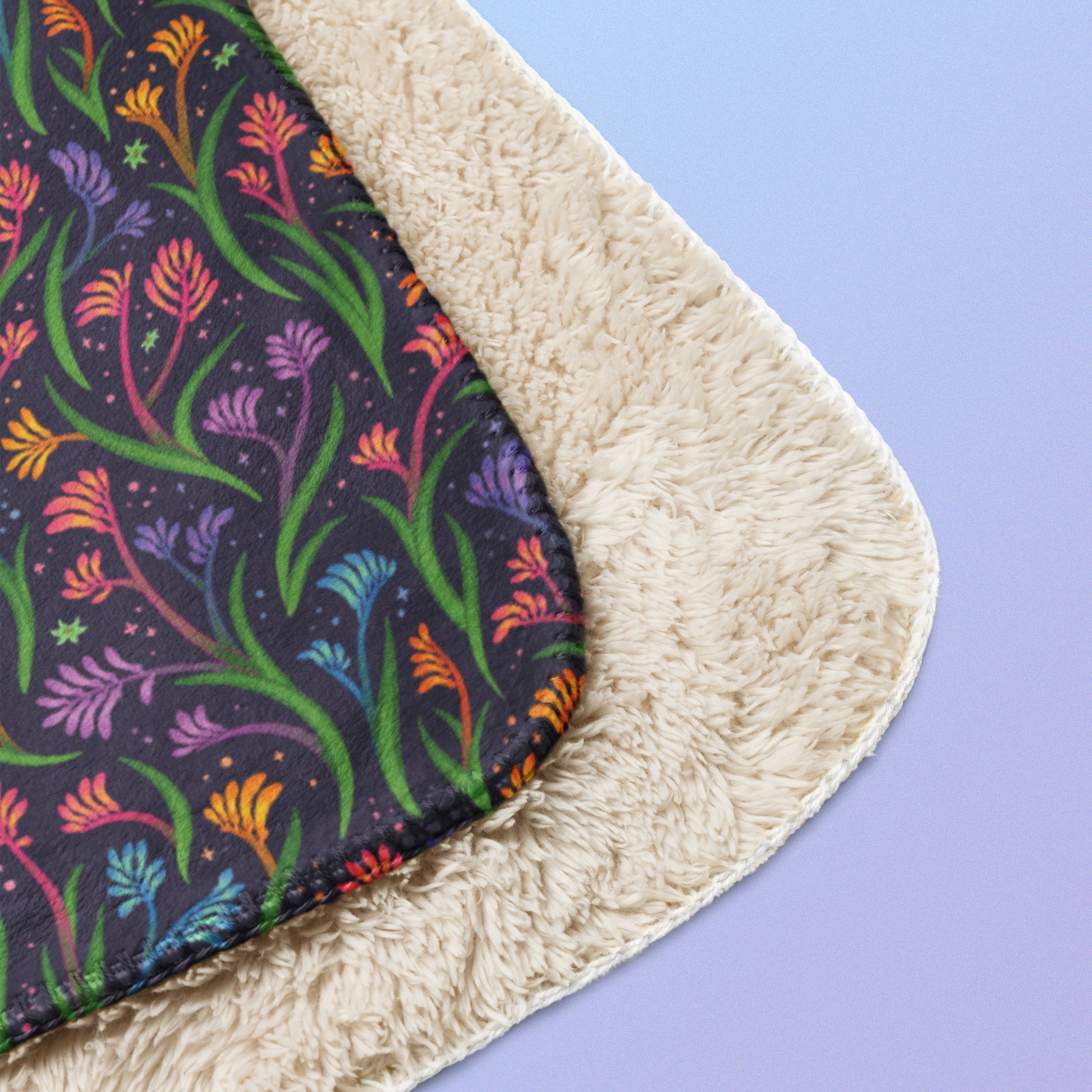 Close up detail of a folded rainbow kangaroo paw flower pattern blanket on a blue and purple gradient background.