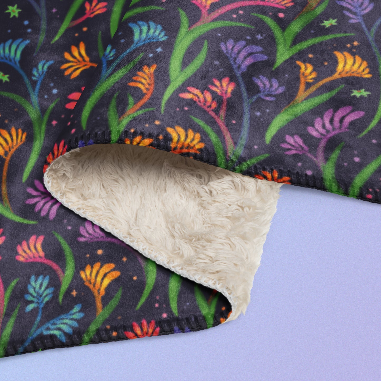 Close up detail of a folded rainbow kangaroo paw flower pattern blanket on a blue and purple gradient background.