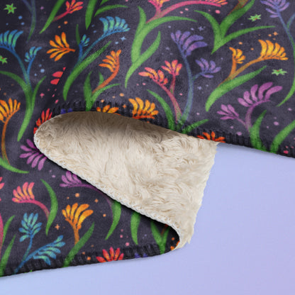 Close up detail of a folded rainbow kangaroo paw flower pattern blanket on a blue and purple gradient background.