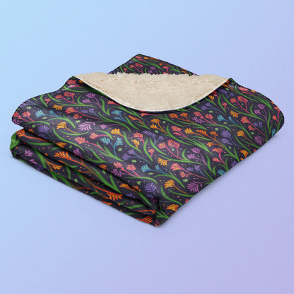 A folded rainbow kangaroo paw flower pattern blanket on a blue and purple gradient background.