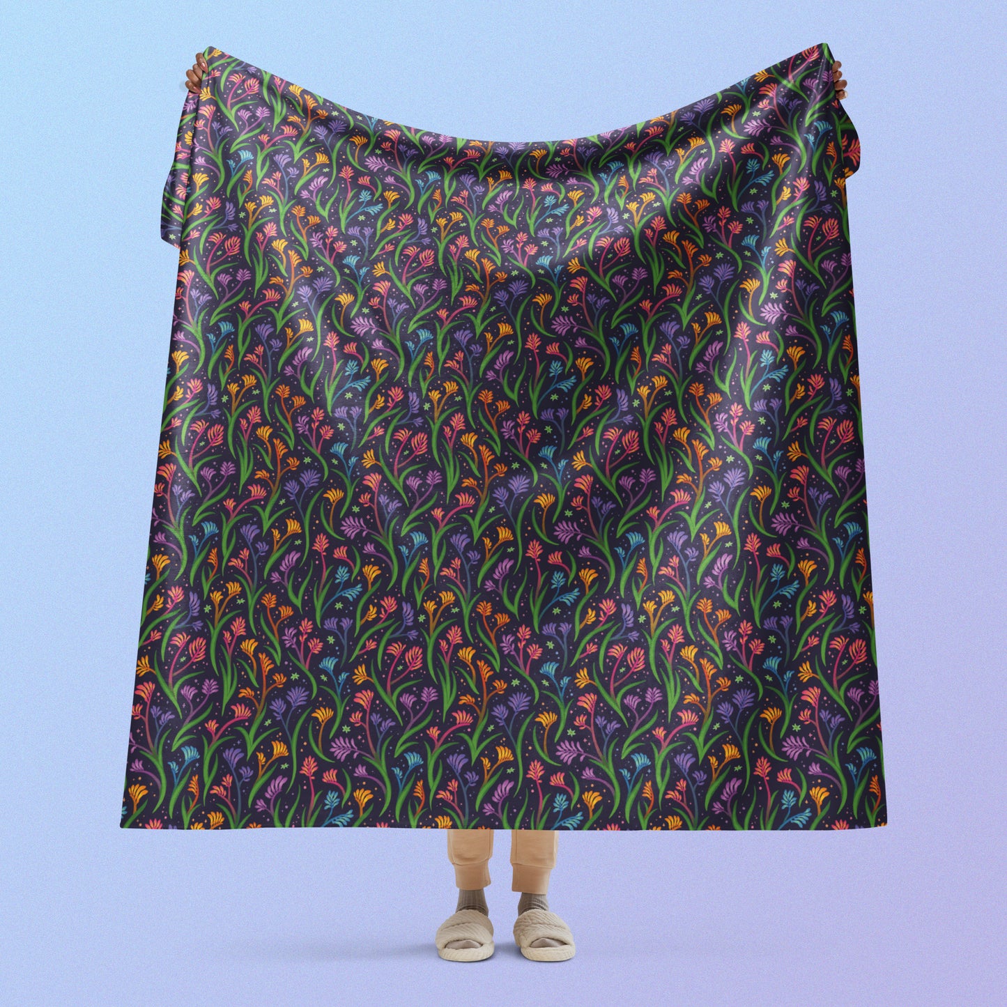 Person holding a rainbow kangaroo paw flower pattern blanket above their head on a blue and purple gradient background.